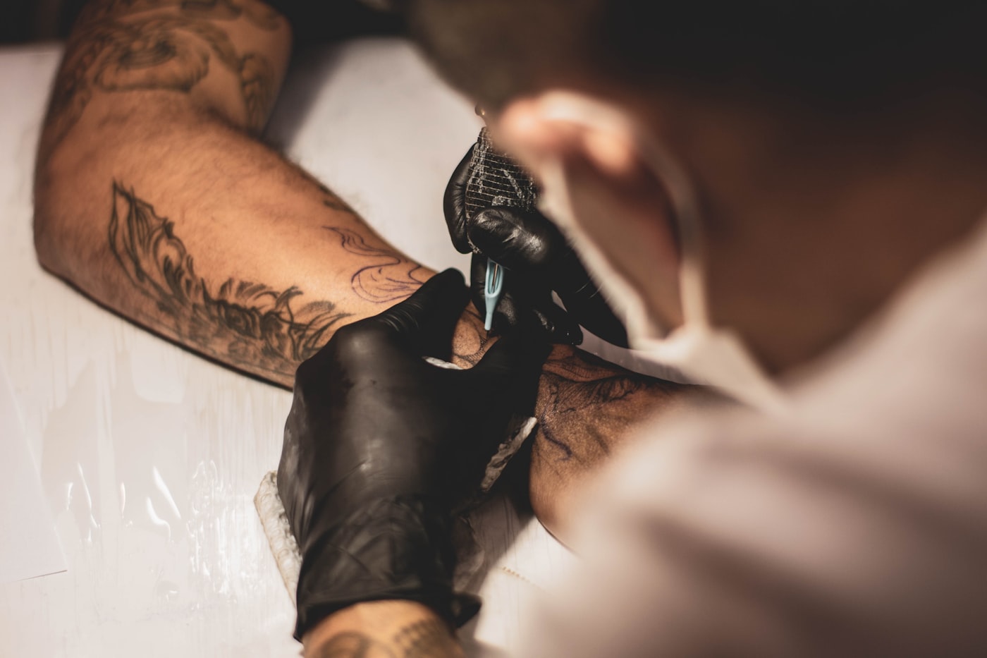 Tattoo artist in black gloves working on a client's arm
